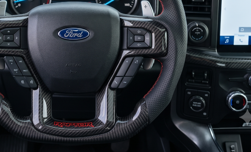 Custom Ford F-150 Raptor carbon fiber steering wheel with red stripe installed in driver cockpit.
