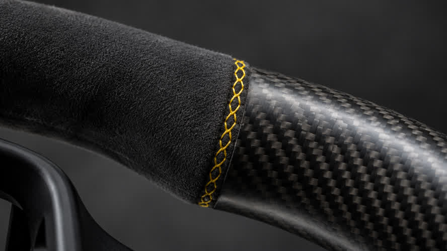 Illustrative charcoal microfiber steering wheel grip with yellow cross stitch beside satin carbon fibre